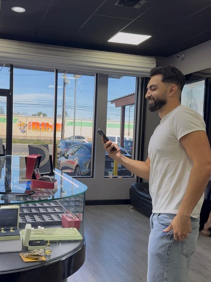 A man in a white t-shirt and jeans checking his phone in a jewellery showroom