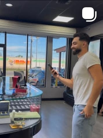 A man in a white t-shirt and jeans checking his phone in a jewellery showroom