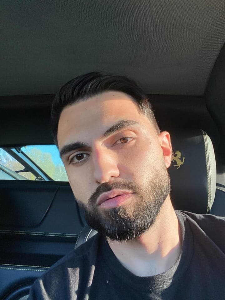 Selfie from the driver's seat, a prancing horse stitched on the headrest behind him, in a black t-shirt